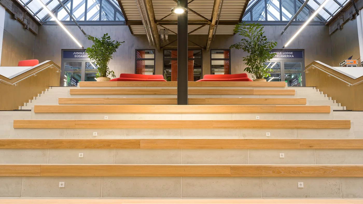 Die breite Sitztreppe aus Holz und Beton mit roten Sofas