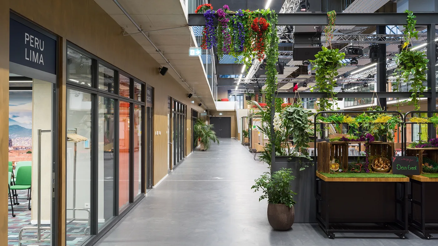 Galerie-Passage entlang der verglasten Meetingräume — mit Blumenampeln
