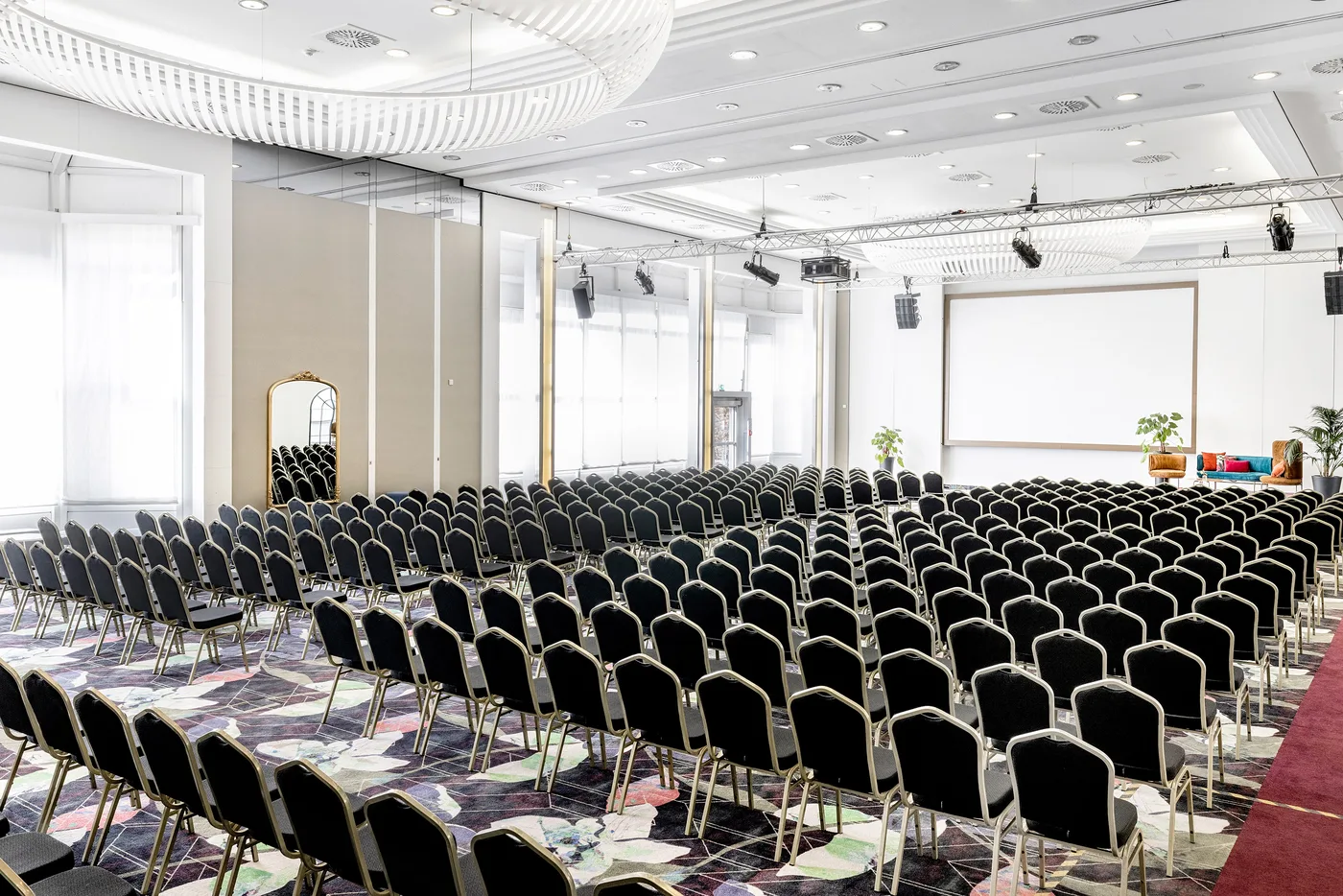 Voll bestuhlter Saal Richtung Leinwand — mit goldgerahmtem Standspiegel