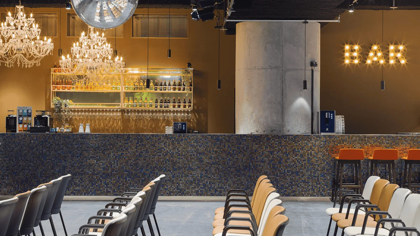 Über die Reihen zur Bar mit Leuchtschrift und Betonsäule